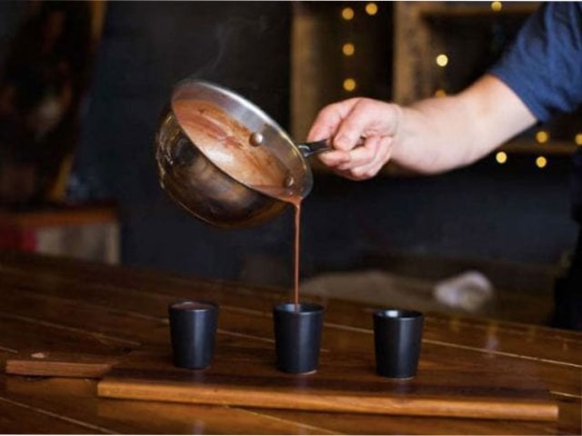 Pouring hot chocolate into three black cups. 