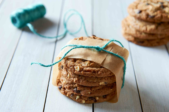 Four chocolate chip cookies stacked on top of each other, with a turquoise string wrapped around them. 