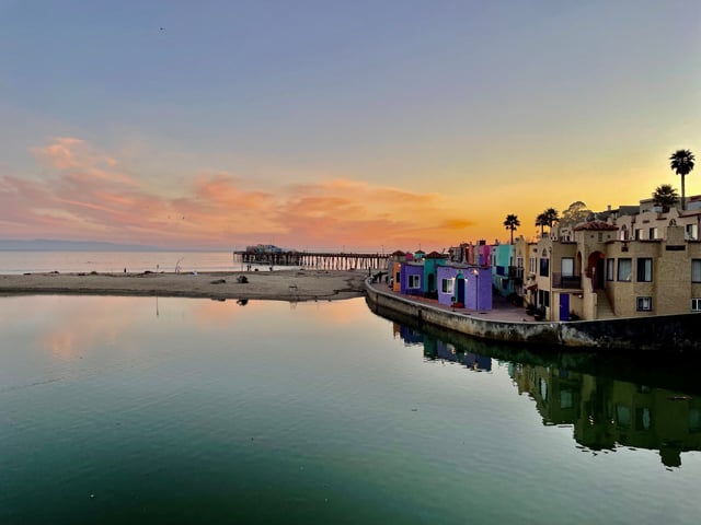 A patio view from Capitola Beach Grill in Capitola Village. The photo overlooks the Soquel Creek River and the Capitola Beach at sunset in Capitola, California.