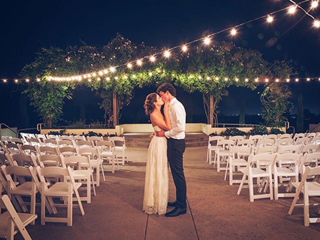 Newly wed couple kissing at Chaminade resort under string lights.