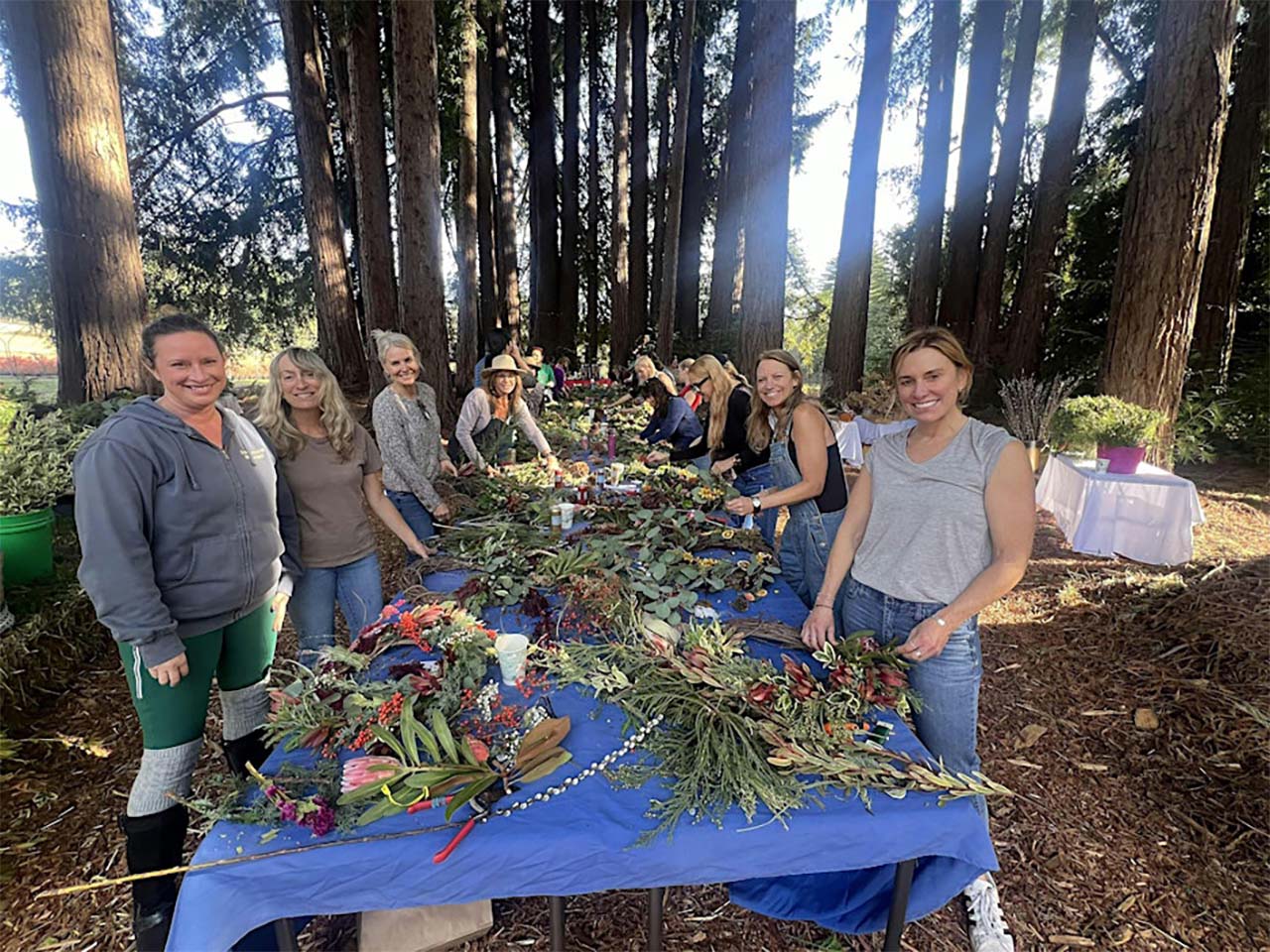 Long table full of wreath builders in a redwood forest