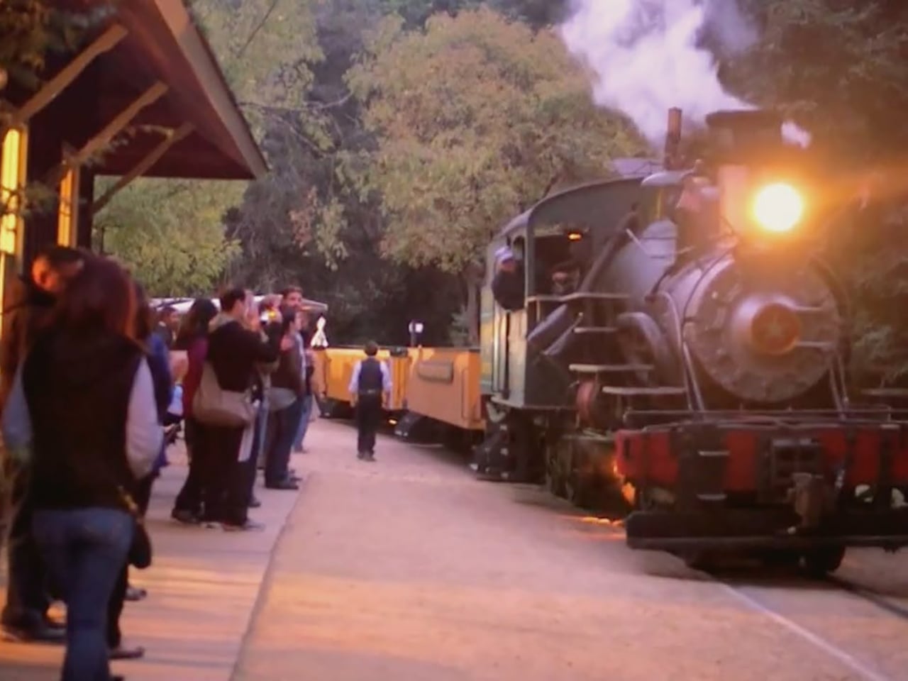 Steam train arriving at a station at dusk with adults waiting to board the train