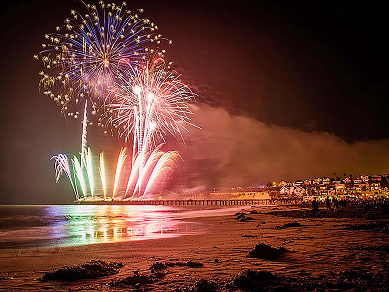Colorful fireworks coming off the Capitola Wharf, lighting up the colorful Venetians and the ocean