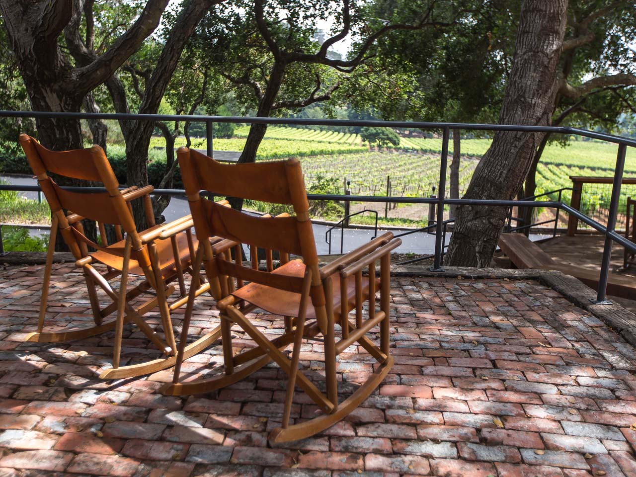 Two rocking chairs on a shady patio overlooking a vineyard.