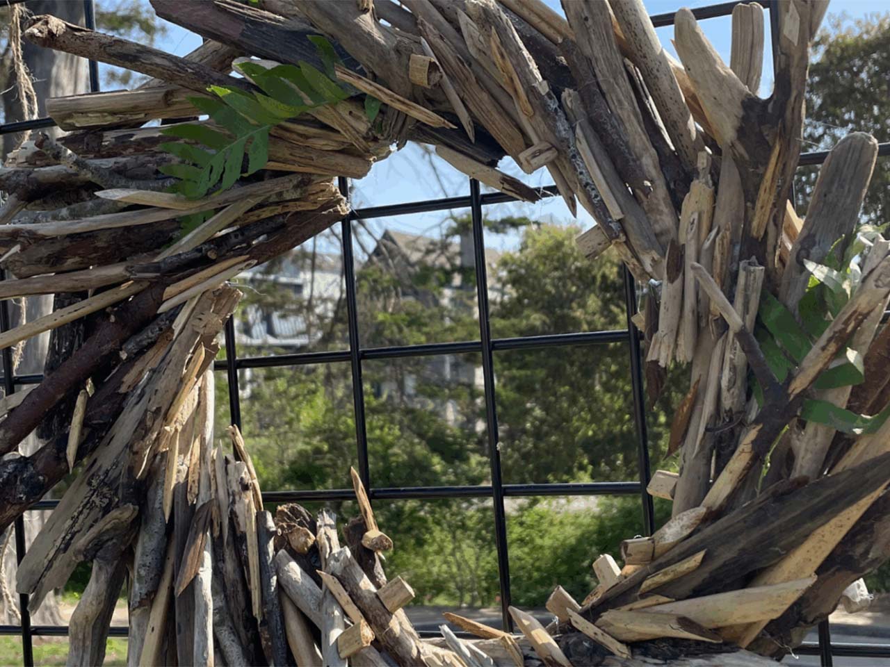 Wreath made of found wood mounted on a fence.