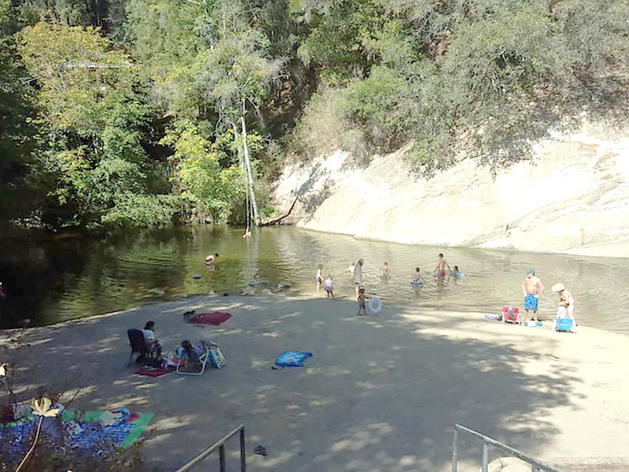 Families on a shady beach and in the water at a swimming hole