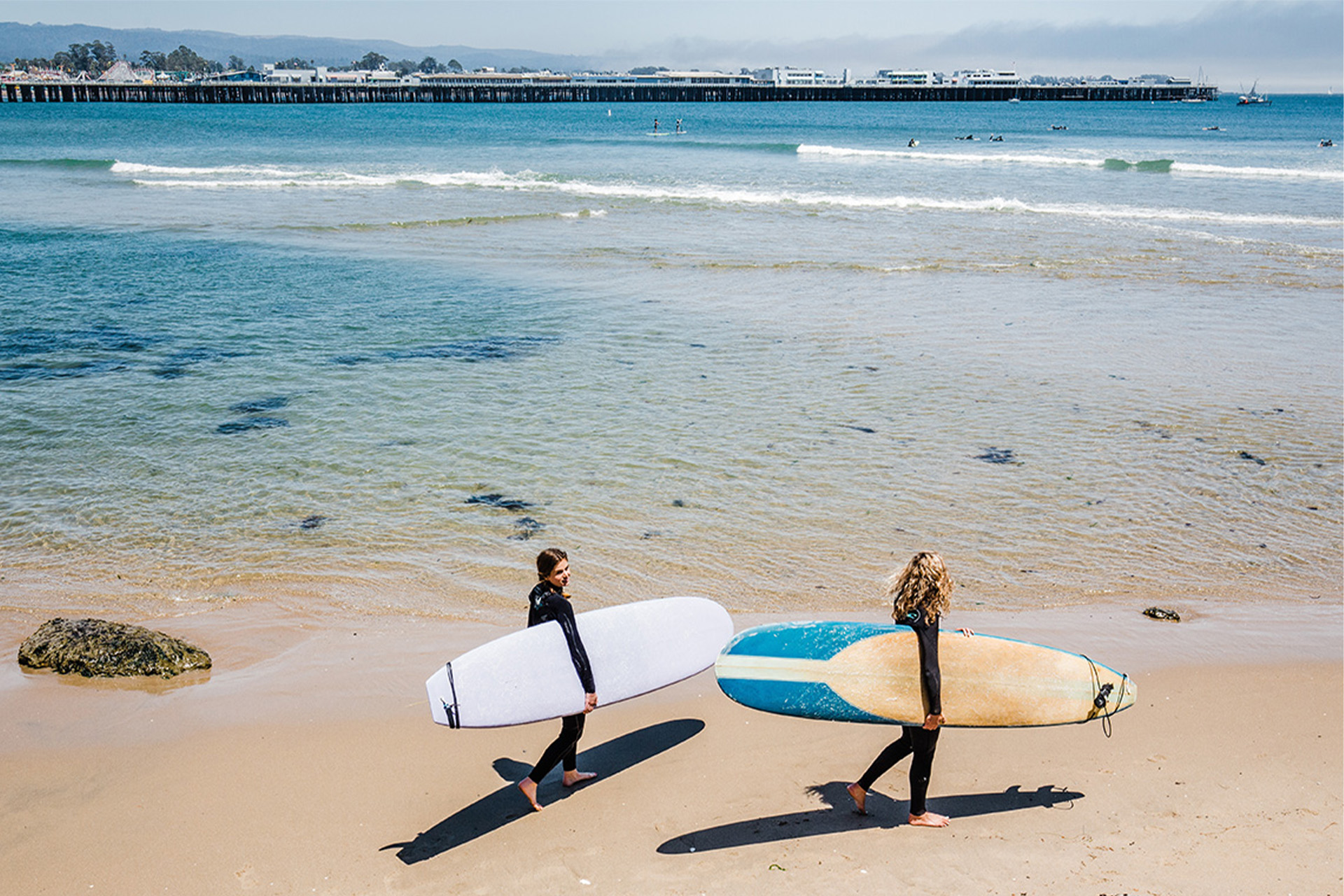 Two surfer girls at Cowell's Beach headed off to surf. Photographed by Impact Creative