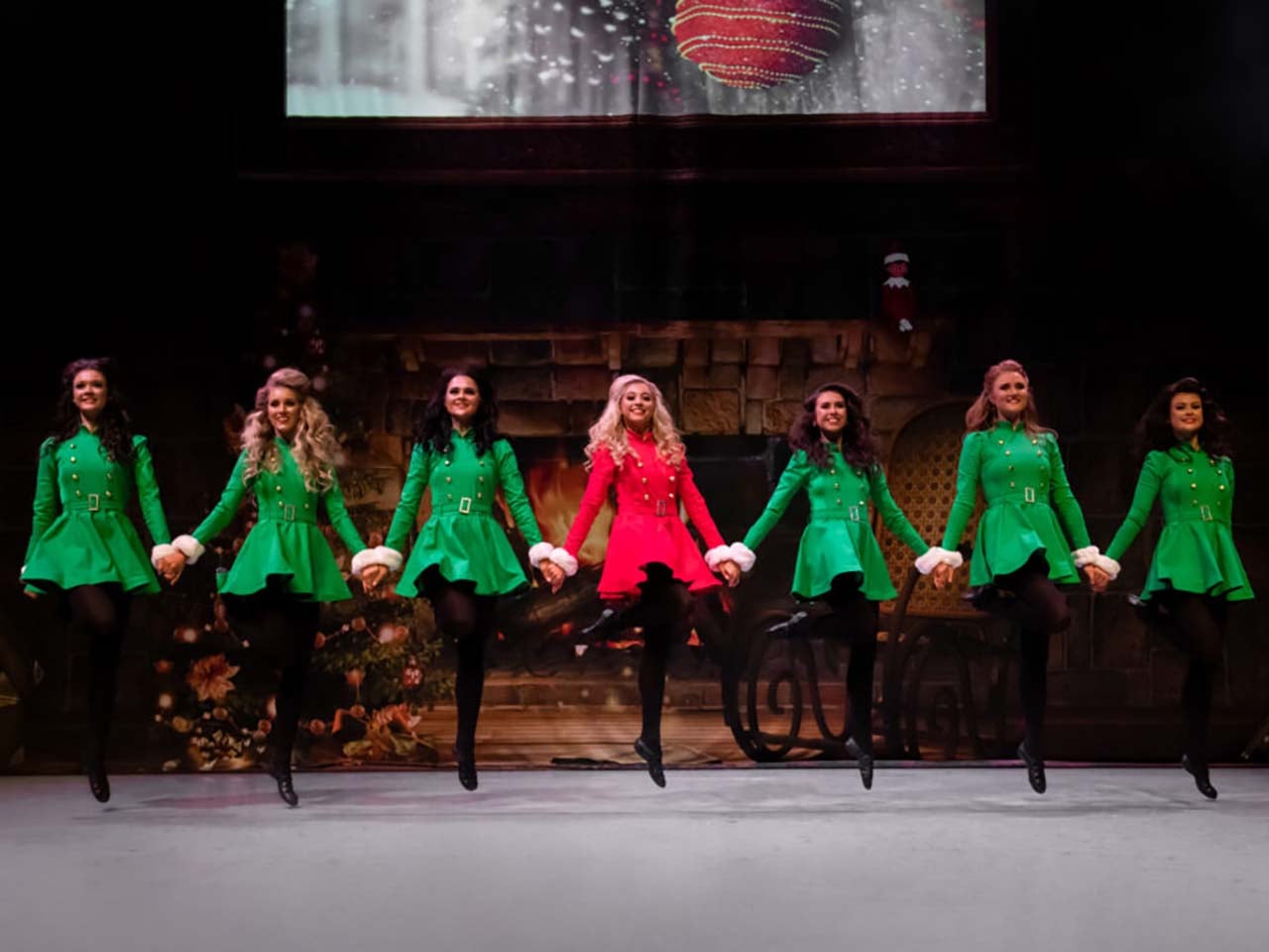 Celtic dancers mid air in red and green costumes in front of Christmas stage designs