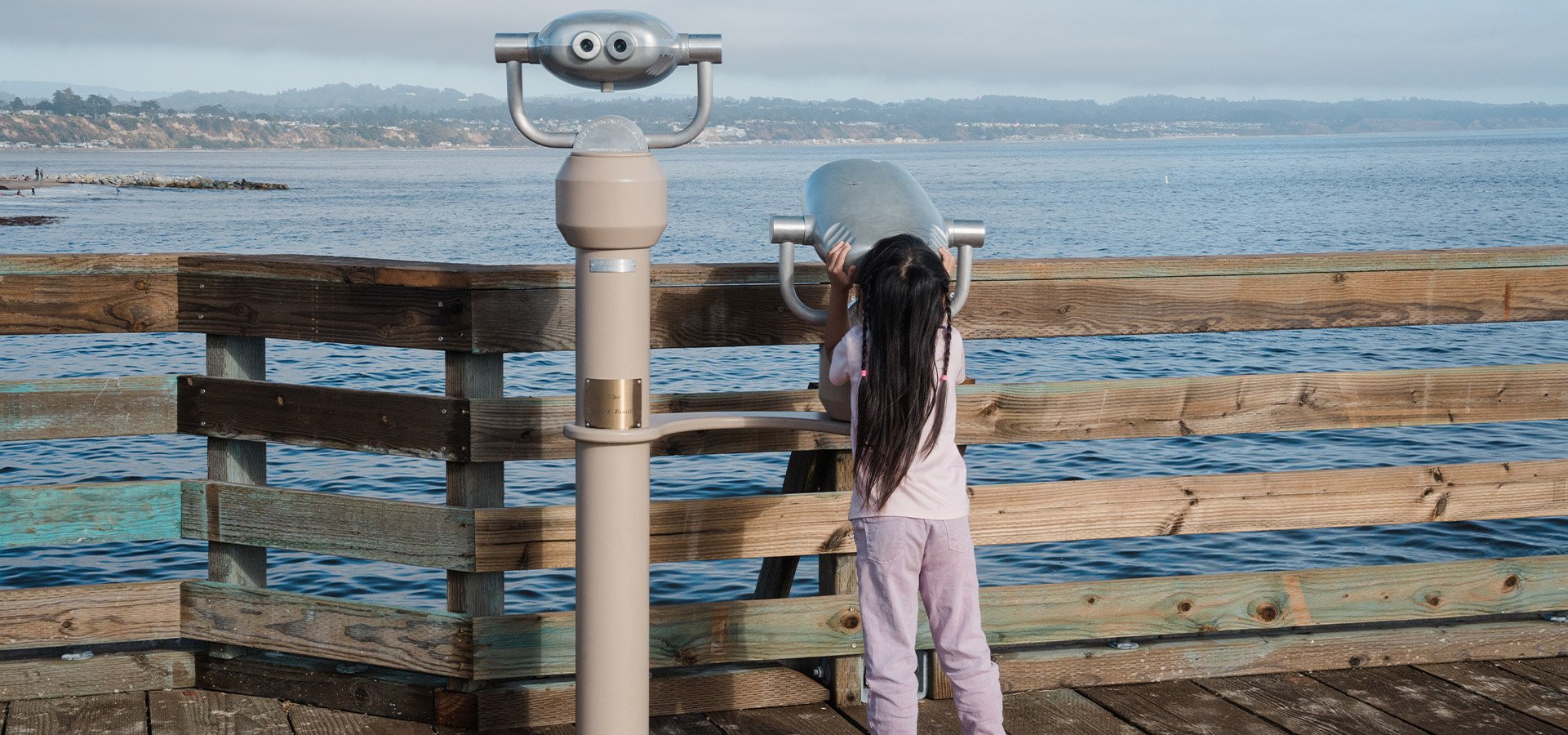 Young individual peering into the binoculars at Capitola. Photographed by Marcus Trawick