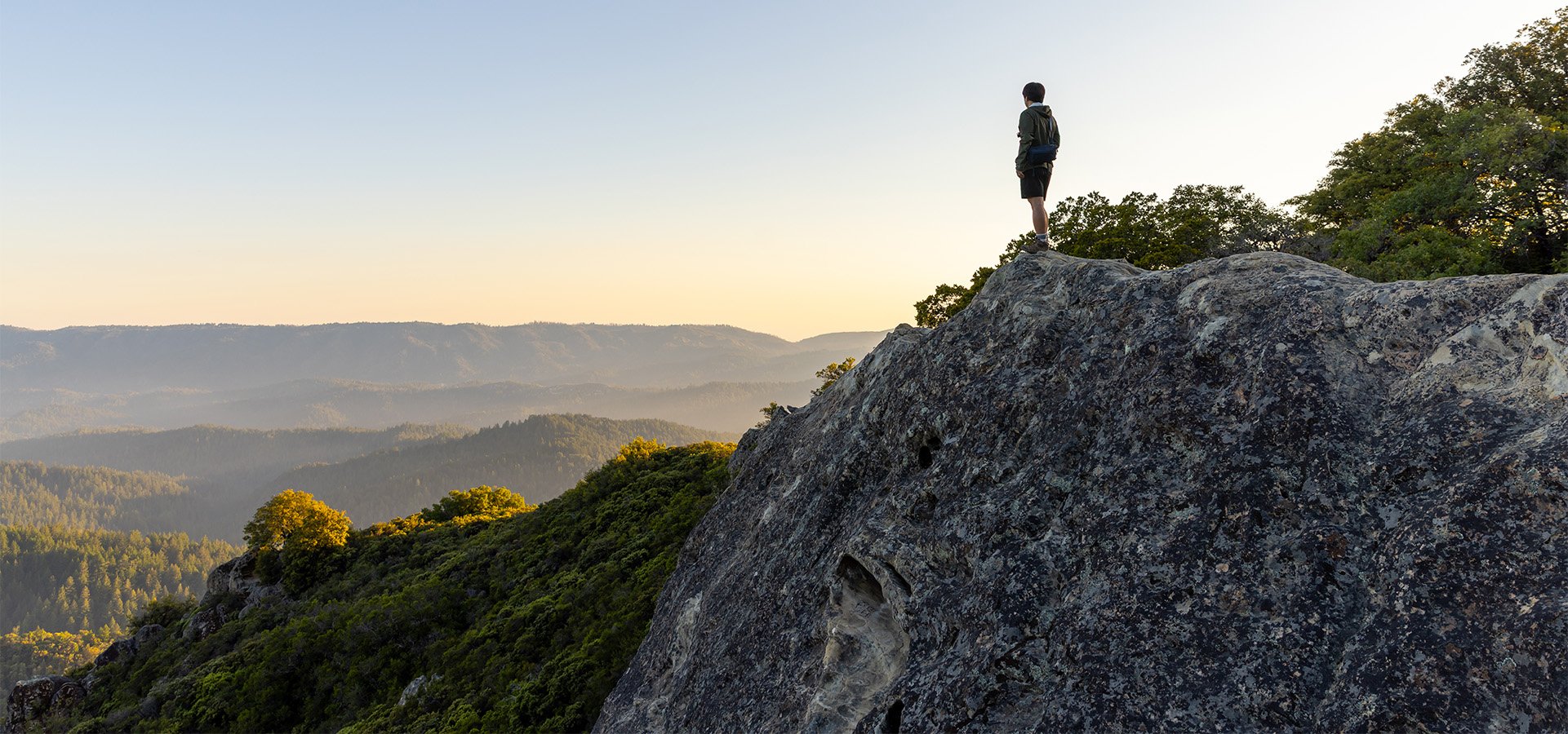 Individual standing at the edge of a rock cliff moments before sunset at Castle Rock State Park. Photographed by Daniel Gorostieta