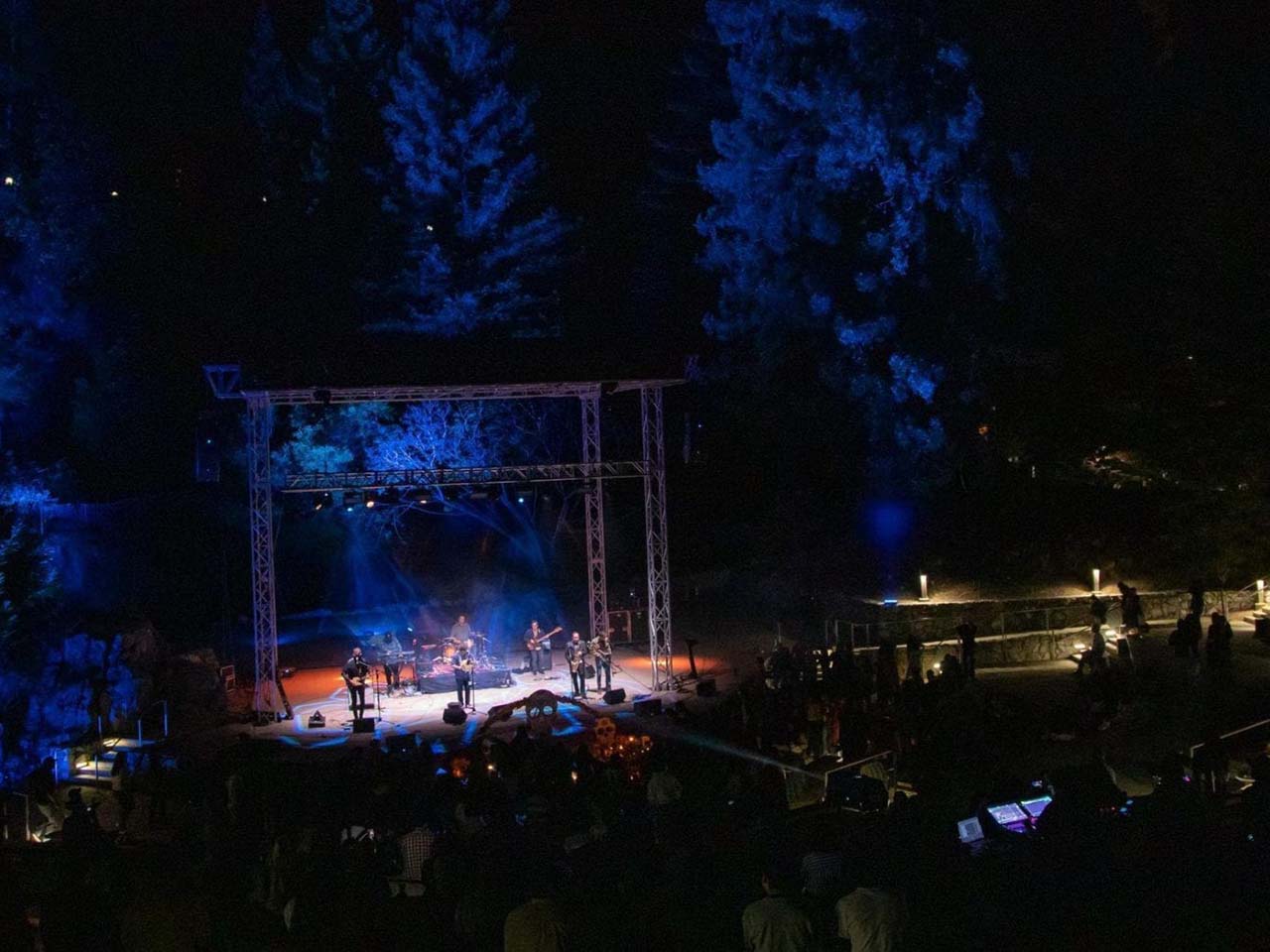 Cultural musicians performing under the lights of a professional stage with a redwood forest and processions around them.