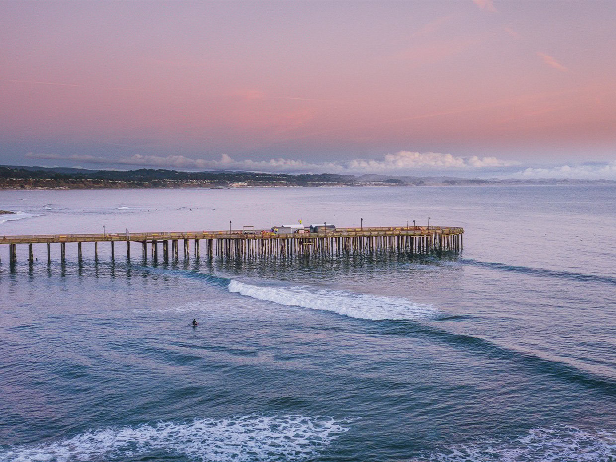 Surfer with the Capitola Wharf in the background during sunrise. Photographed by Liz Birnbaum, The Curated Feast