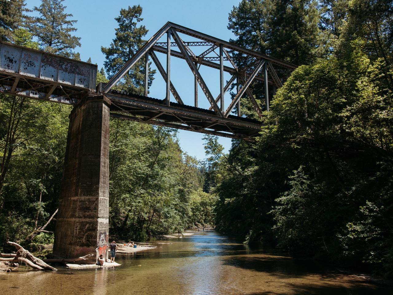 A river beach next to an old train bridge over the river.