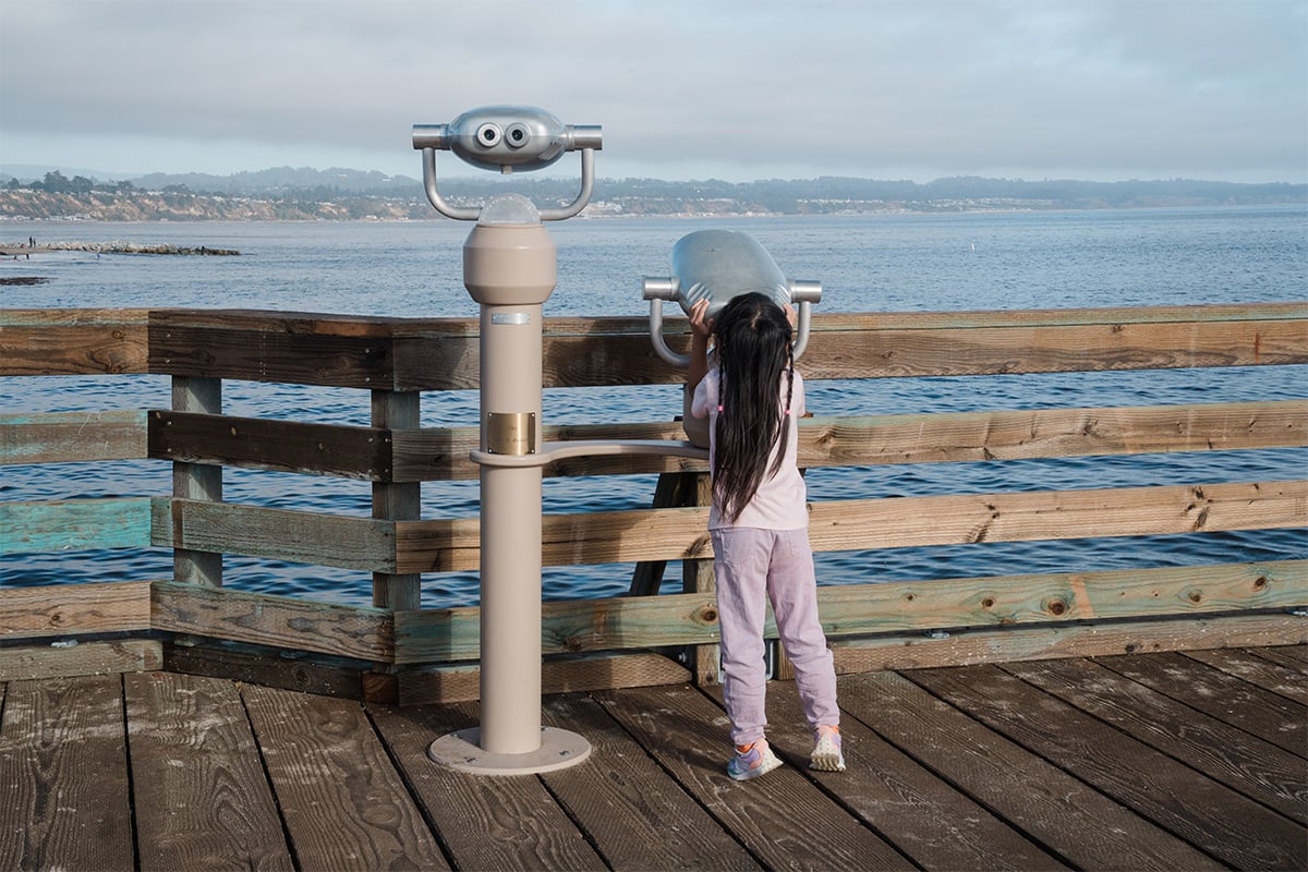 A young child peering into the binoculars at the Capitola Wharf. Photographed by Marcus Trawick