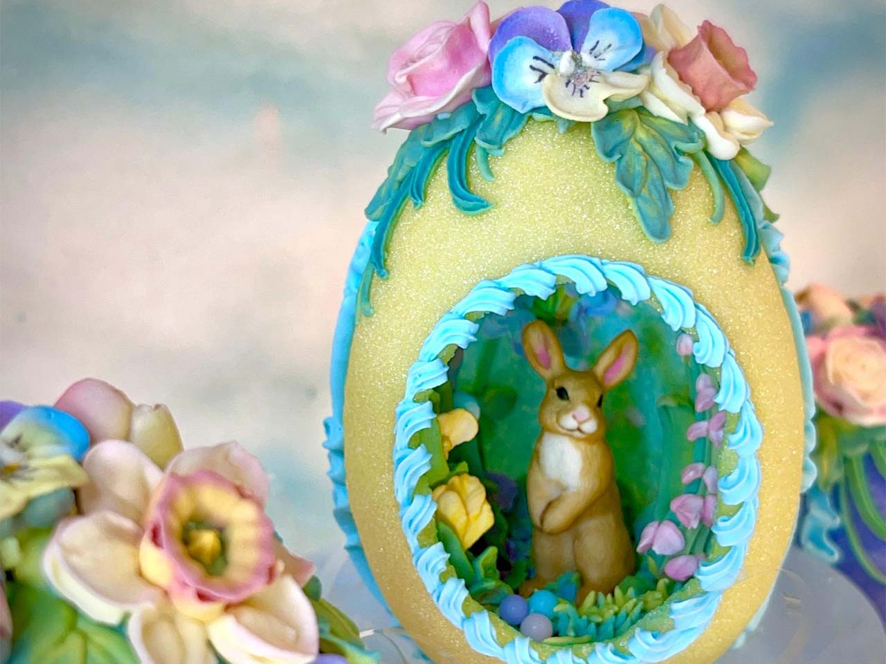 A hallow egg with a decorative hole showing a bunny and flowers all made out of edible sugar.
