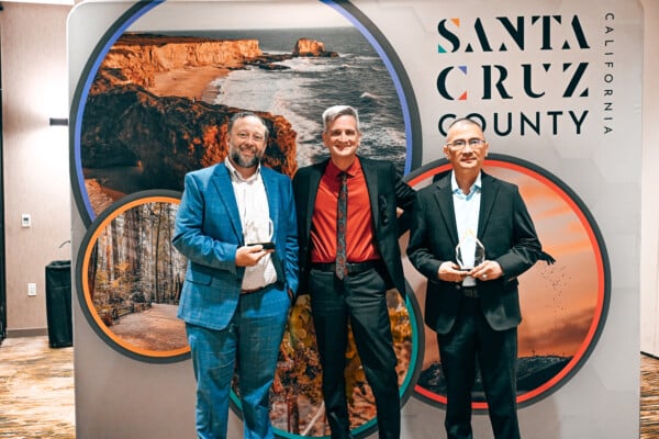 Visit Santa Cruz County CEO, Terence Concannon, Director of Operations, Greg Liversedge and General Manager of La Quinta, Herman Wuysang in front of the Visit Santa Cruz County banner
