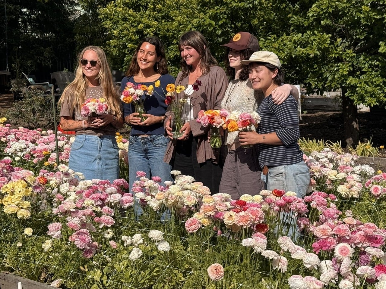 Women in a field of flowers, holding bouquets of flowers.