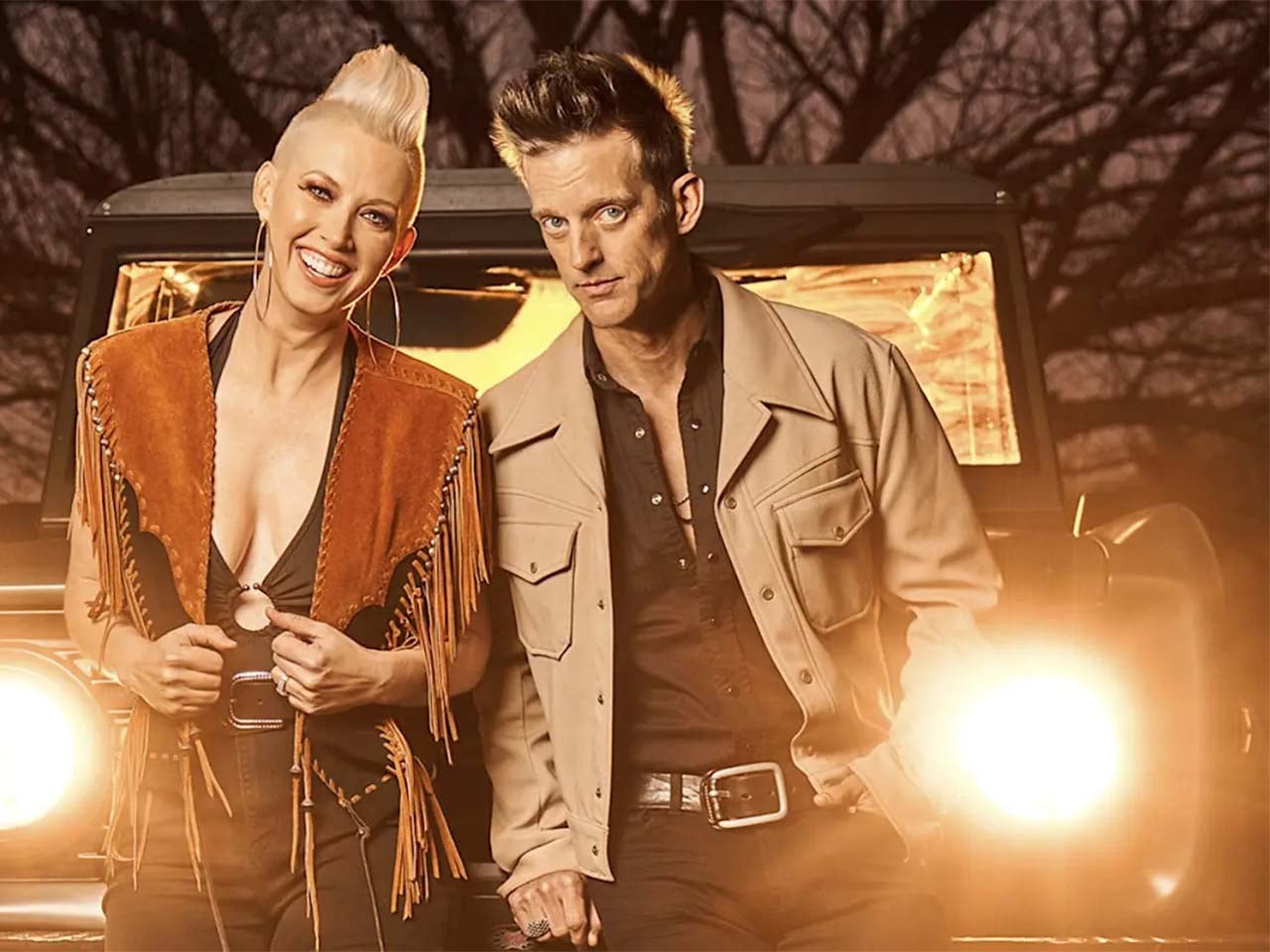 Country duo standing in front of bright jeep headlights