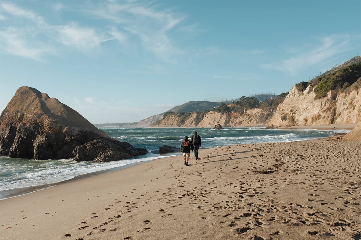 Two people walking down the beach at Greyhound Rock. Photographed by Desi Wishart