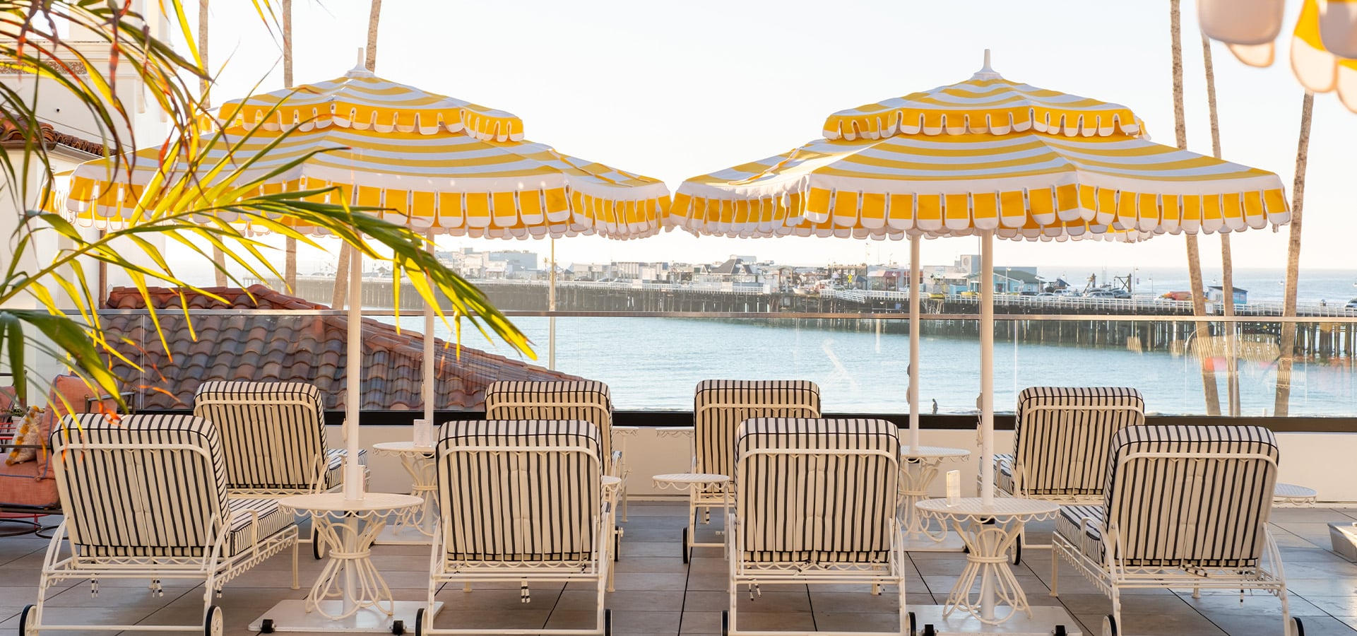 Pool Deck lounge chairs and yellow with white striped umbrellas overlooking the Santa Cruz Wharf and Monterey Bay. Photographed by Daniel Gorostieta