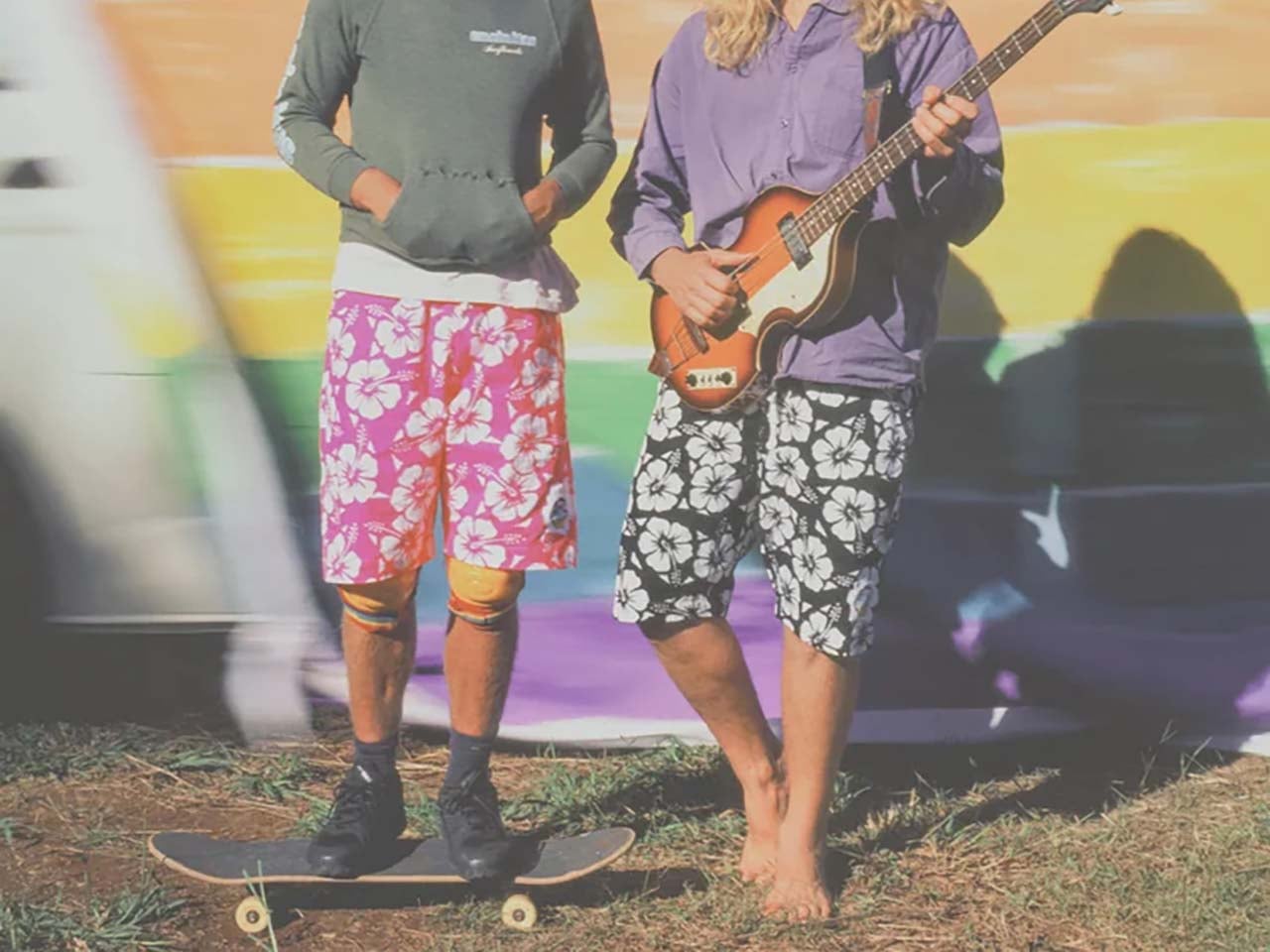 The feet of the performers. One holding a guitar and the other on a skateboard.
