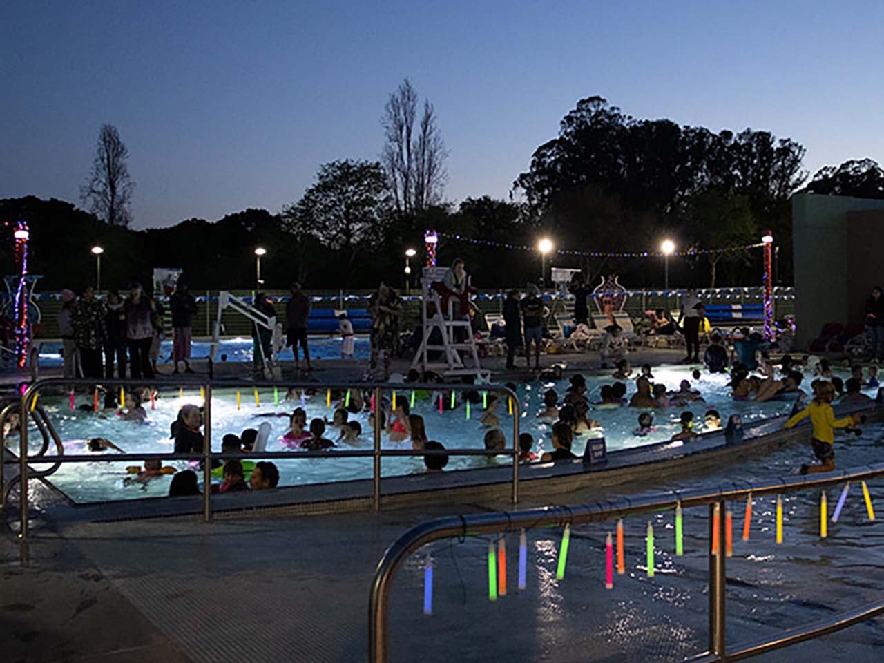 Families playing in a pool with glowing decorations around them at night