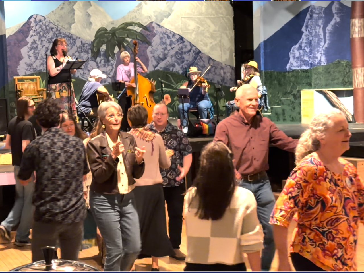Folk musicians on a stage calling out a room full of people contra dancing.