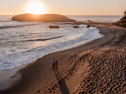 Two people walking along the beach of Greyhound Rock during sunset. Photographed by Ben Ingram